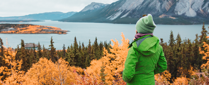 Hiker woman in green outerwaer at autumn fall mountains landscape.